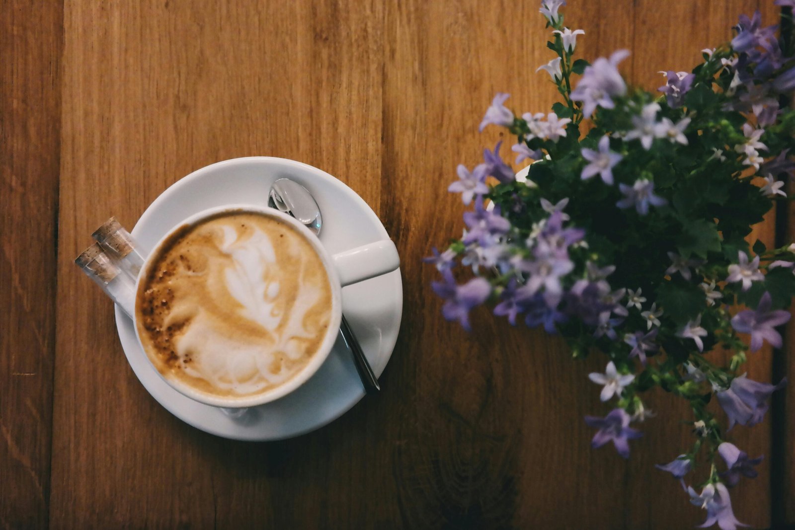 A beautifully crafted cappuccino paired with delicate purple flowers on a wooden table.