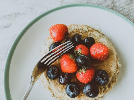 Stack of pancakes topped with fresh strawberries and blueberries on a plate.