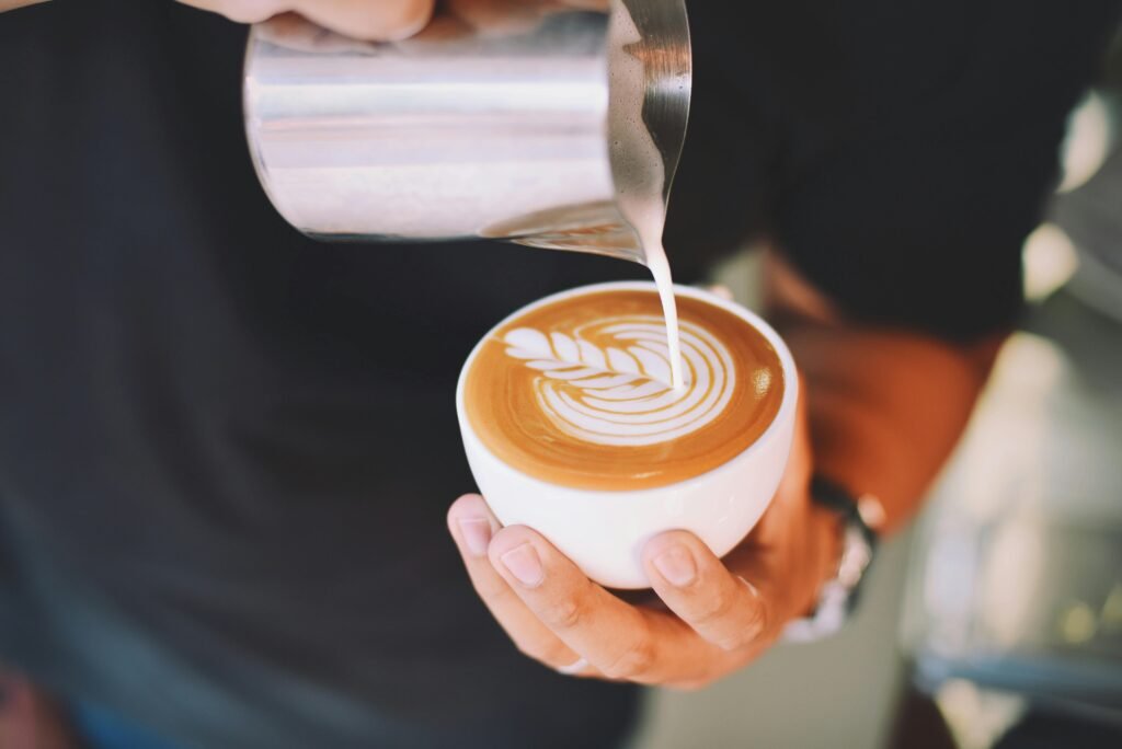 Close-up of a barista pouring latte art into a coffee cup indoors.