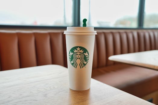 A Starbucks coffee cup on a wooden table inside a cozy cafe setting with warm lighting.