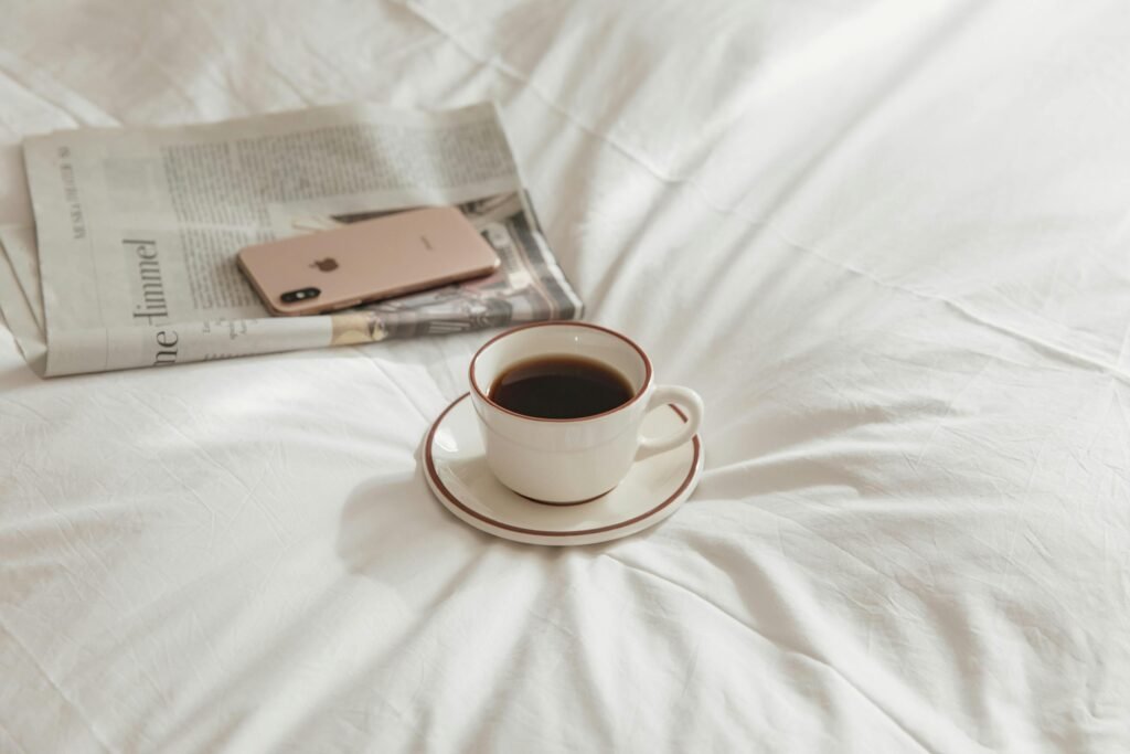 A cup of coffee on bed with a smartphone and newspaper.