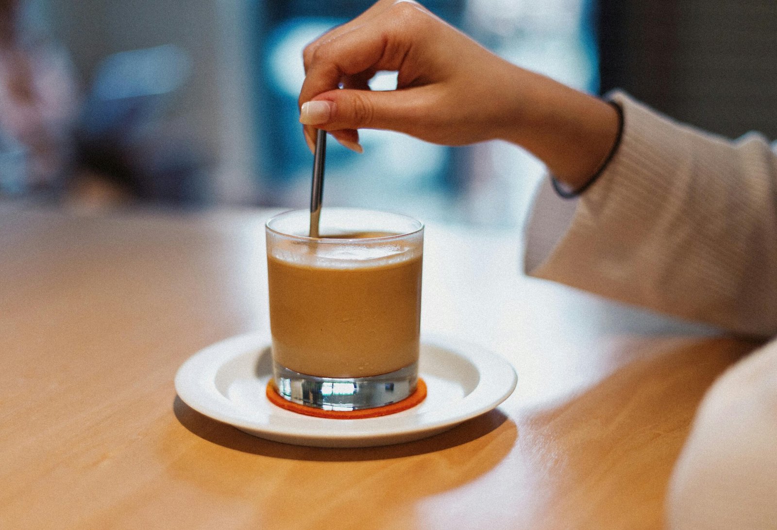A warm indoor cafe scene in Shinjuku, Tokyo, featuring a hand stirring a glass of coffee on a wooden table.