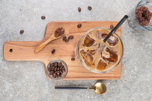 Top view of a refreshing iced coffee with straw on a wooden board, accompanied by coffee beans and a golden spoon.