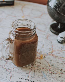 High angle of glass jar with warm cocoa drink placed on map on table