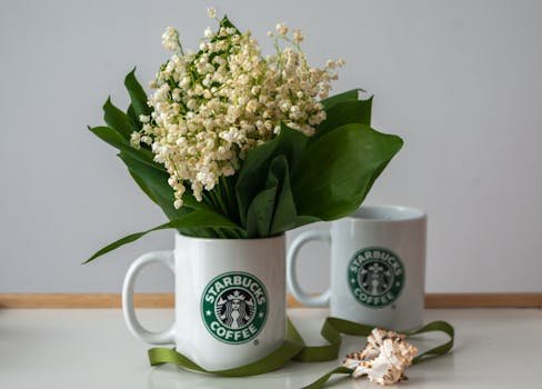 Lily of the Valley arrangement in a Starbucks mug on a table with decorative elements.