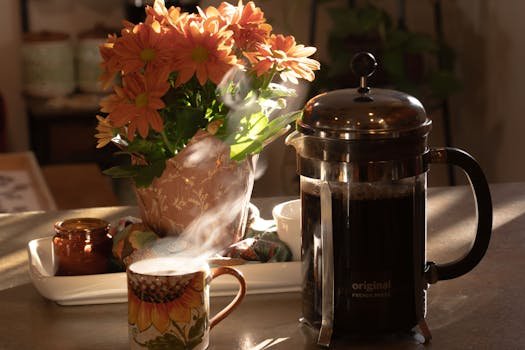 A warm morning scene with coffee, flowers, and a French press on a table.