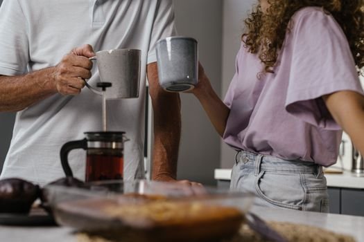 Couple enjoying a morning tea, holding mugs over a kitchen counter. Perfect start to a day.