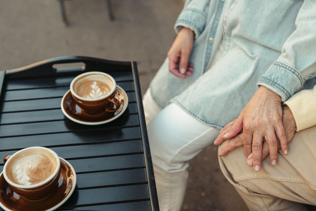 A couple enjoys coffee and intimate moments, holding hands at an outdoor café.
