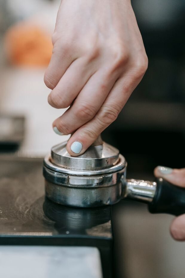 Coffee terms for beginners espresso terms explained A close-up of a barista's hand tamping espresso grind in a portafilter, emphasizing precision.