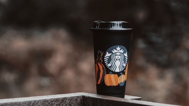 Reusable coffee cup with pumpkin design outdoors in autumn setting.